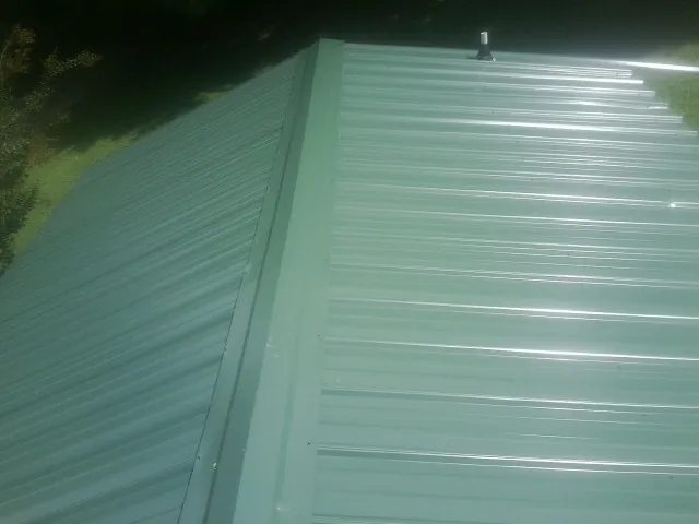 New green metal panels meeting at the ridge of a roof — Flat Roof Repair work by our crew in Altoona