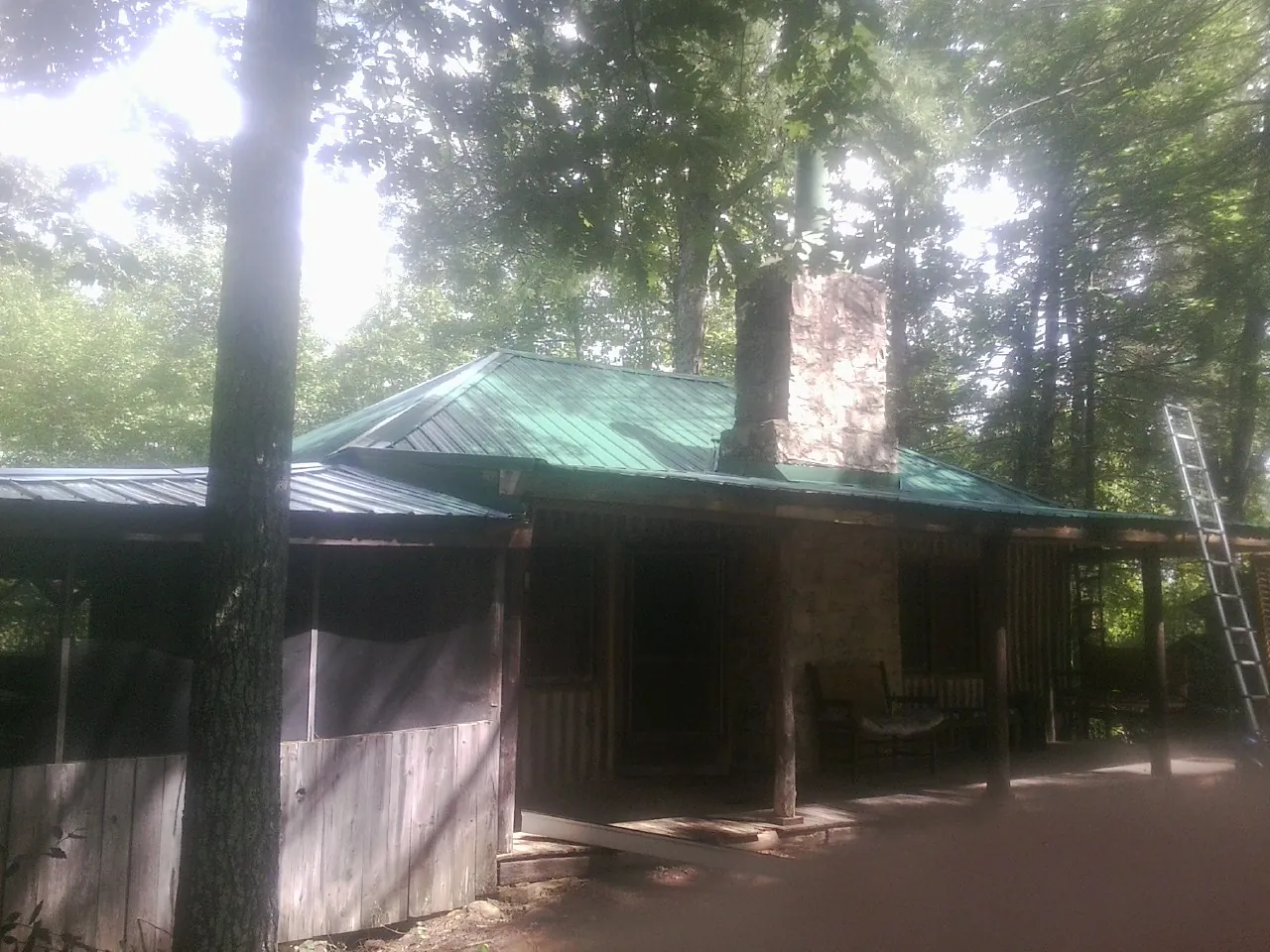 Green metal roof and stone chimney above a log cabin porch in Altoona