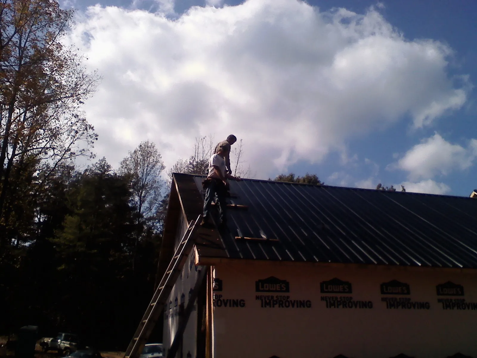 Roofer fastening dark metal panels high against a cloudy sky, from a Roof Inspection job in Altoona