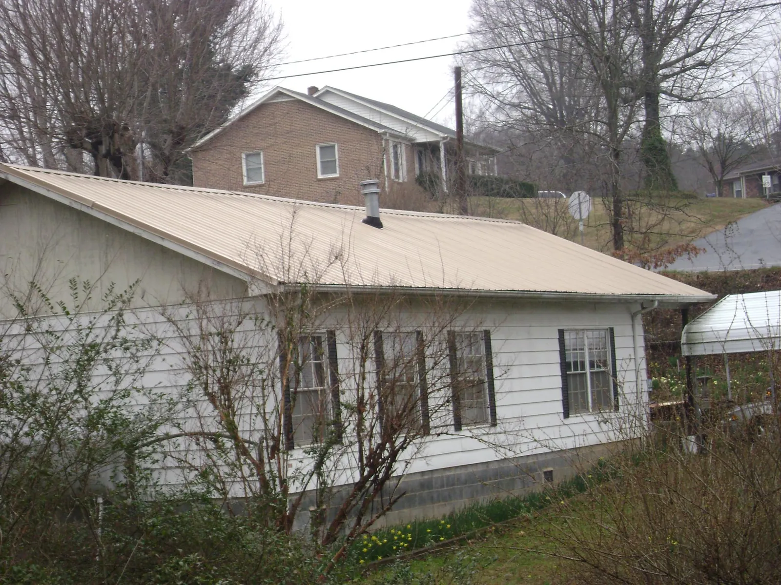 Tan metal roof on a white sided house set into a hillside — Commercial Roofing by Roofing Brothers in Altoona
