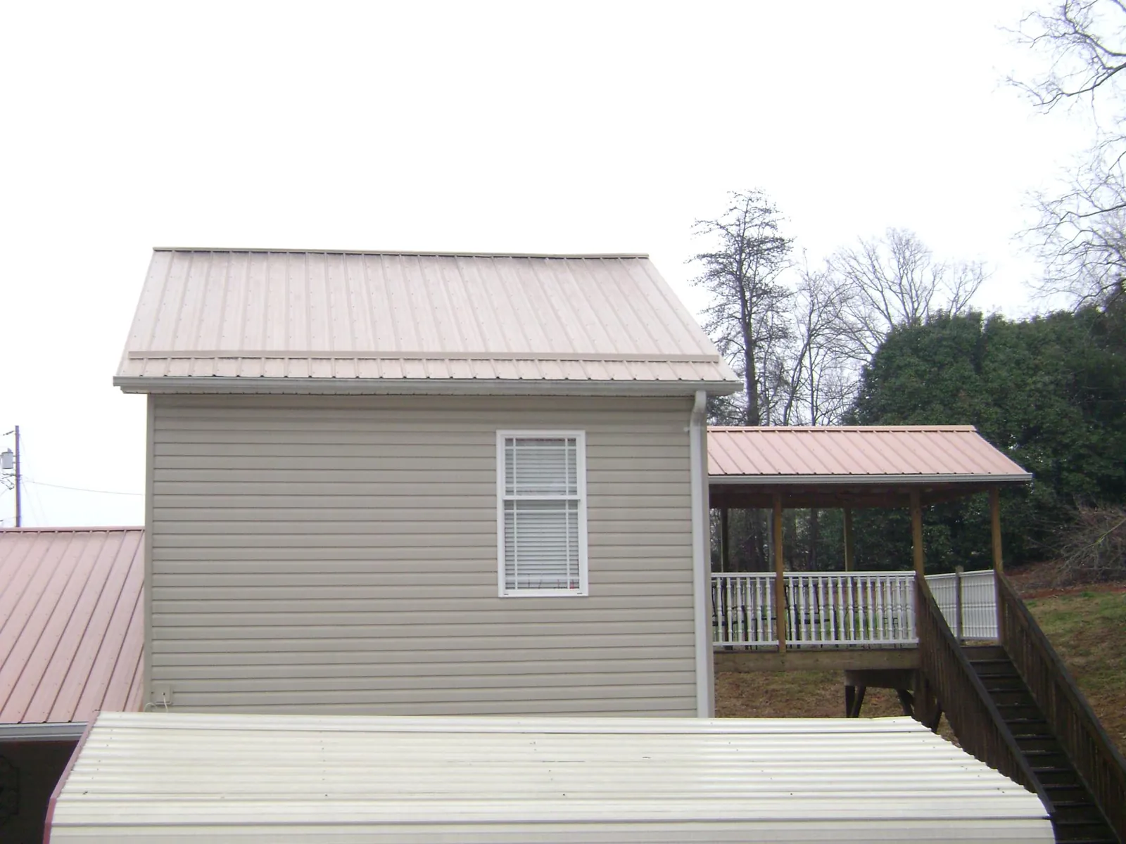 Tan metal roofs on a two story addition and attached porch, from a Roof Replacement job in Altoona